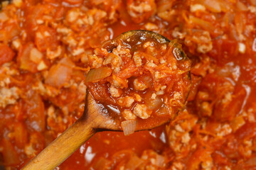 The image is a close-up of a wooden spoon holding ground meat, onion, and tomato sauce