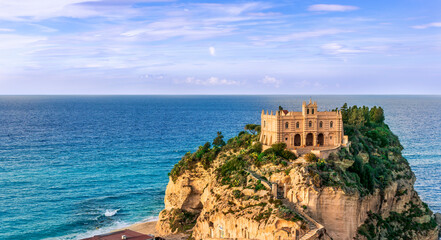 sea landscape of beautiful white temple or castle on a high cliff isle on a rock in crystal clear turquoise sea with waves and beautiful sunset or sunrise on background of seascape
