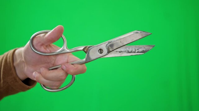 An active and functional mood is captured as a hand firmly holds open a pair of well-used, large tailor's shears against a vibrant green screen. It's ideal for showcasing craftsmanship, tailoring