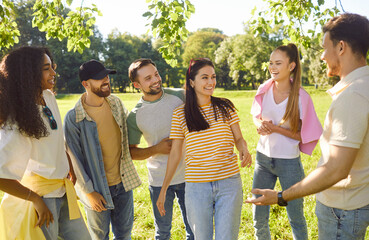Outdoor shot of cheerful friends meeting together in park, discussing something, standing in...