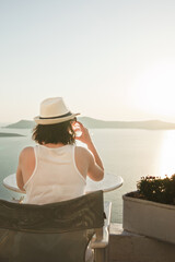 A woman enjoys a scenic sunset view over the Aegean Sea from a Santorini terrace with a glass of wine.