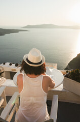 A woman enjoys a scenic sunset view over the Aegean Sea from a Santorini terrace with a glass of wine.