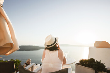A woman enjoys a scenic sunset view over the Aegean Sea from a Santorini terrace with a glass of wine.