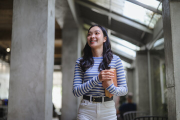 Happy student walking in university corridor holding a book