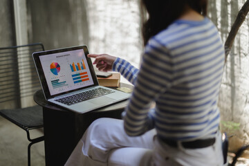 Businesswoman analyzing business reports on laptop, pointing at screen with finger