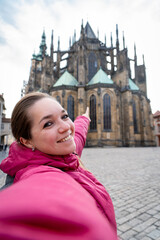 Mujer turista tomándose una selfie en frente de la Catedral de Praga, señalando hacia ella.