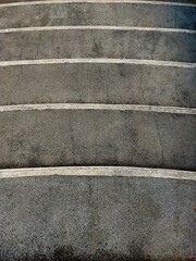 A close-up, high-angle view of gray concrete steps with subtle white lines, creating a repetitive and abstract pattern. Highlights the rugged yet simple aesthetic of urban design 