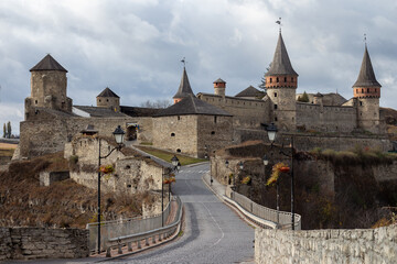 The historic Kamianets-Podilskyi Castle in Ukraine is approached via its ancient stone bridge, showcasing the impressive fortifications and a cloudy sky above this iconic medieval landmark.