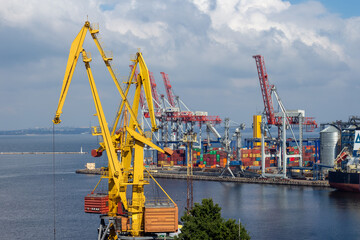 A wide shot shows the busy Port of Odesa Ukraine featuring towering gantry cranes moving numerous brightly colored shipping containers, with the city visible in the background, maritime industry