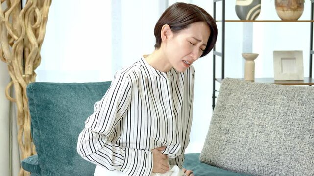 ソファに座りお腹をおさえる女性