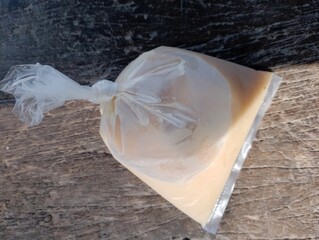 Sealed translucent plastic bag containing sweet milky liquid on wooden surface