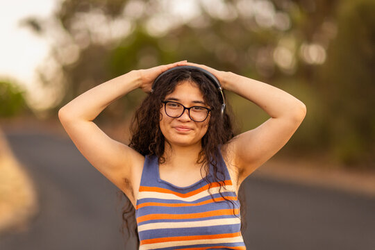 teen girl wearing headphones and glasses with hands on her head showing hairy armpits