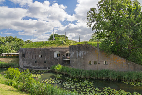 Fort Vuren, a historic Dutch fortress surrounded by a moat and lush greenery, under a beautiful sky with fluffy clouds. Part of the Dutch Water Lines.