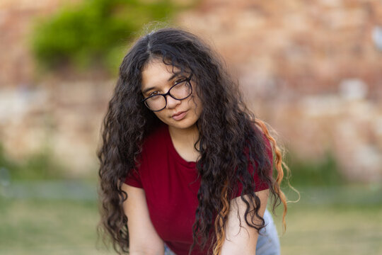 teenaged girl with glasses leaning forward with long dark curly hair falling over her shoulders