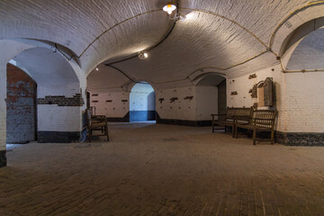 Inside Fort Vuren: a vast, vaulted brick chamber with arched doorways and wooden benches, lit by old-fashioned bulbs. Part of the Dutch Water Lines.