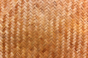 View of a finely woven bamboo mat or surface, displaying a classic diagonal or herringbone pattern. The natural light brown and golden tones of the bamboo create a warm and inviting texture.