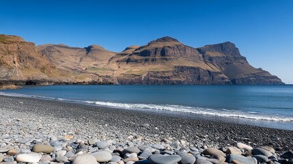 Serene coastal scene featuring a pebble beach, gentle waves, and imposing, rugged mountains under a clear blue sky