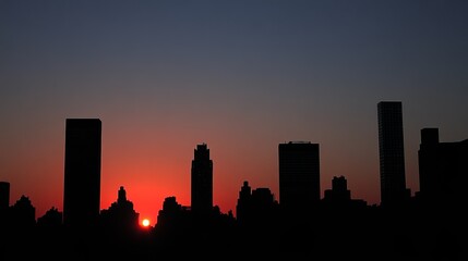Silhouette of a city skyline at sunset, with the sun partially obscured by buildings.  Red hues dominate the sky