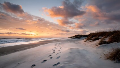 Obraz premium A wide sandy beach stretches out towards the horizon under a sky filled with soft pink and orange hues at sunset