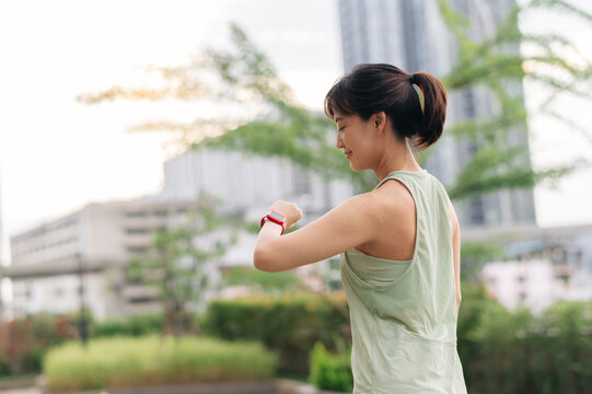 Focused asian woman in 30s check pulse heart rate result on smartwatch wristwatch after fitness workout exercise. Healthy lifestyle wellness healthcare technology in urban city at sunset