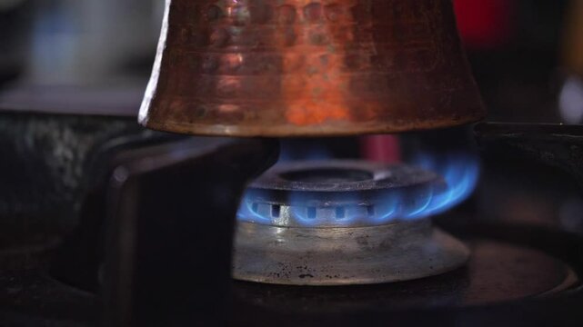 A warm and functional mood is captured as a traditional copper pot rests on a gas stove burner, clearly showing the steady blue flame underneath. This shot is ideal for depicting cooking