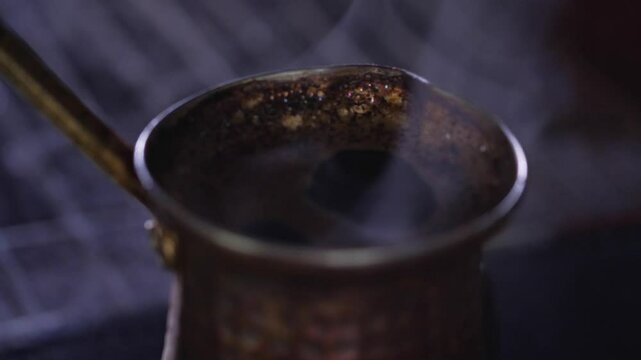 An aromatic and traditional mood is captured as dark, rich Turkish coffee simmers with a delicate foam and steam rising from a classic copper cezve pot