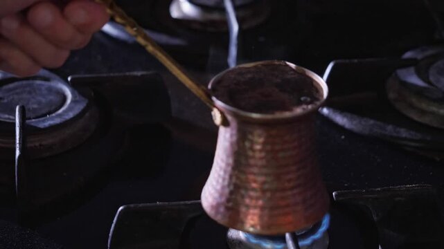 An authentic and ritualistic mood is captured as a hand holds a traditional copper cezve pot over a blue gas flame, actively brewing Turkish coffee. This shot is ideal for depicting cultural culinary 