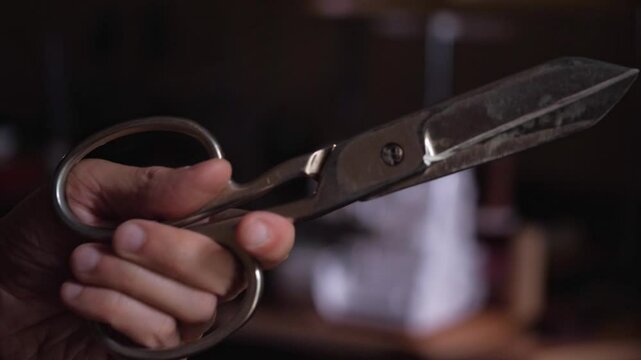 A strong and ready mood is captured as a hand firmly holds a large pair of closed tailor's shears, suggesting precision, craftsmanship, or the anticipation of cutting