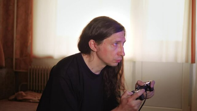 An intensely focused and engaged mood is captured as a man with long hair plays a video game, his gaze fixed on the screen, reflecting deep immersion and concentration
