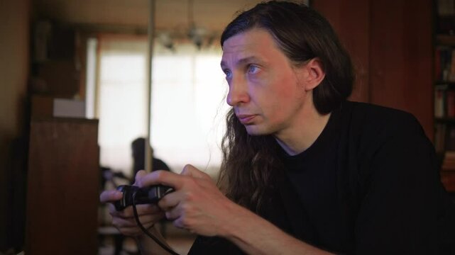 An intensely focused and engaged mood is captured as a man with long hair plays a video game, his gaze fixed on the screen, reflecting deep immersion and concentration