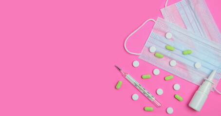  Antiseptic thermometer, pills and a protective medical mask,on a pink background, on a flat surface. 