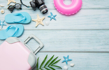 Pink suitcase, blue flip flops, pink lifebuoy and camera resting on light blue wooden background