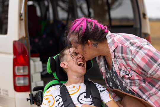 Mother giving her son with disability on a wheelchair a kiss