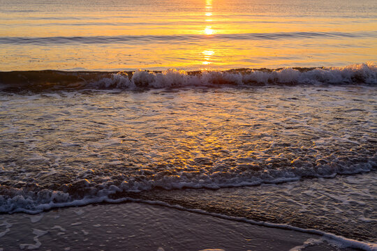 Golden reflections at water's edge at dawn with small waves