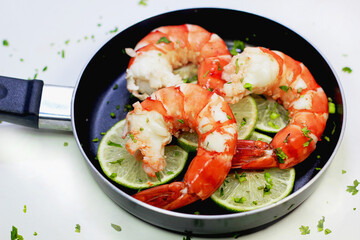Boiled Black Tiger Shrimps with Tails on Thin Lemon Slices and Chopped Thai Coriander in Black Pan on White Background