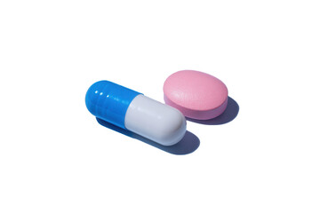 Vibrant blue and white capsule next to a soft pink tablet against a seamless backdrop creating a soothing contrast