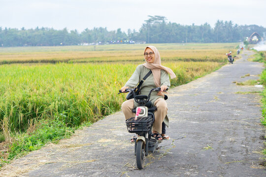 Mother and daughter ride electric bike together in rice field outdoor