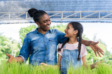 African mother and daughter care for seedlings on trays at organic farm. Family relationships,...