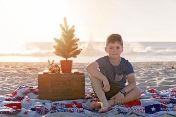 Pre Teen Boy Sitting In a Christmas Themed Setting At The Beach At Sunset