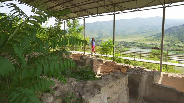 Female traveler sightseeing overlooking the preserved ruins of the King's Bath at Armaziskhevi site, surrounded by green hills and valley in Mtskheta region