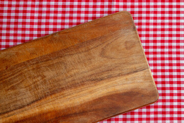 wooden cutting board on tablecloth red-white scotch pattern. top view