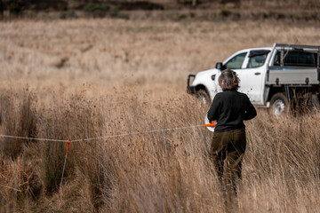 female farmer reeling a electric fence a farm putting up a steel post fence with high tensile wire in australia women working in agriculture farming in spring