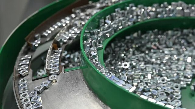 Slow motion scene the vibration blow feeder operation with zinc plate square nuts.