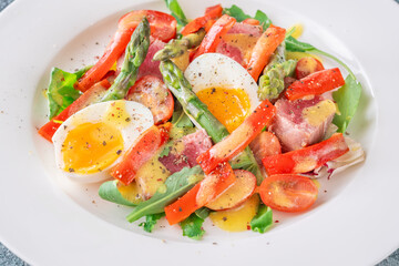 Elegant Niçoise portion with eggs, tuna, arugula, asparagus, cherry tomatoes, white plate
