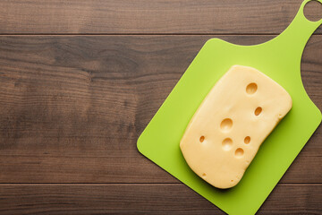 Flat lay photo of big piece of cheese on green plastic cutting board with copy space.