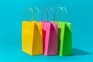 Shopping paper bags on the turquoise blue background. Minimalist photo of pink, yellow and green bags. Isometric view of shopping paper bags with central composition as summer sale concept.