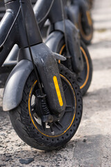 Closeup photo of front wheel of scooter. Concept of urban transportation. Many electric scooters parked in a row in a sidewalk in the city.