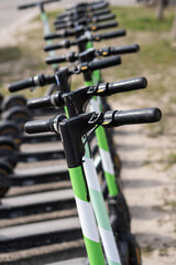 Closeup photo of handle bars of electric scooter. Many electric scooters parked in a row in a sidewalk in the city. Closeup photo of battery-powered rental scooters.