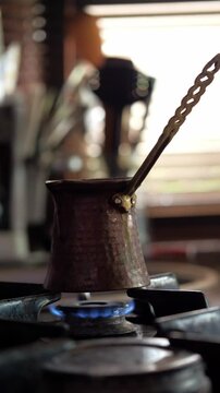 An authentic and aromatic mood is captured as Turkish coffee is brewed in a traditional cezve pot over a blue gas flame. This shot is ideal for depicting cultural culinary practices, the art of coffee