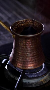 An aromatic and traditional mood is captured as dark, rich Turkish coffee simmers and brews in a classic copper cezve pot on a gas stove, with subtle steam rising